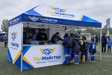Шатер з друком на футбольному полі, під ним діти в спортивній формі