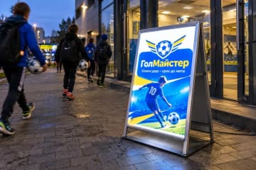 Штендер з підсвіткою біля спортивної школи, поруч діти з м'ячами