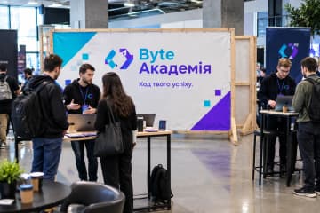 На технологічній конференції показано брендвол Wood з дерев’яним каркасом і ПВХ-банером поруч із столом для демонстрацій.