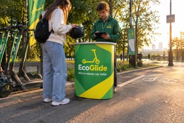 Промостіл Oval розміром 60×51 см на пункті прокату електросамокатів просто неба, де видно овальну стільницю та друковану панель спереду.