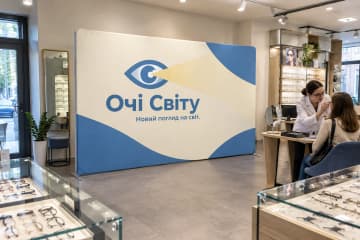 Прямий текстильний поп-ап 450×230 см для бренду «Очі Світу» в оптиці поруч із вітринами окулярів і консультаційним столом.