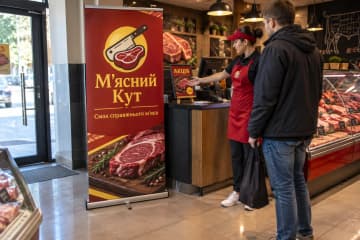 У м’ясному магазині М'ясний Кут стоїть рол-ап Junior 100×200 см з тонкою касетою та одним полотном, поруч із касою та покупцем.