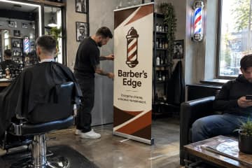 У барбершопі Barber's Edge показано рол-ап Junior 80×200 см з тонкою касетою та одним полотном біля крісел і дзеркал.