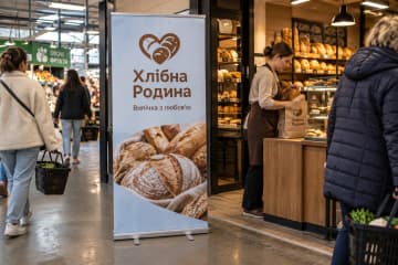 На фото ролл-ап Classic розміром 80×200 см стоїть біля входу до пекарні на продуктовому ярмарку, видно алюмінієву касету та дві поворотні ніжки.