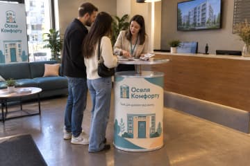 Телескопічний промо-стіл з LED-підсвіткою та друкованою передньою панеллю розміщений у лобі офісу оренди квартир біля ресепшена.