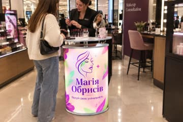 Телескопічний промо-стіл з LED-підсвіткою та друкованою фронтальною панеллю стоїть у магазині косметики біля дзеркал і тестерів.