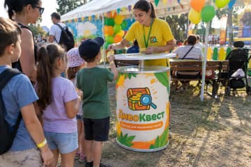 Телескопічний промо-стіл з LED-підсвіткою та друкованою передньою панеллю стоїть на сімейному фестивалі в дитячій зоні біля намету та лавок.