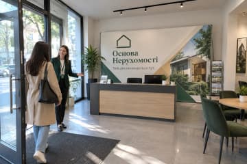 На фото текстильний стенд Тексвол 225×600 см в офісі агентства нерухомості біля рецепції та стільців для клієнтів.