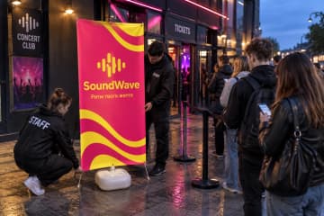 Поруч із входом до концертного клубу стоїть Х-банер Outdoor 100×200 см на важкій водонаповнюваній основі.