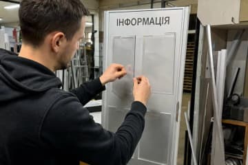 Майстер вклеює прозору кишеню в інформаційний стенд на виробництві